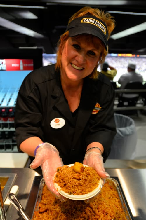 A smiling Cajun Corner team member holding a fresh bowl of jambalaya at the Caesars Superdome